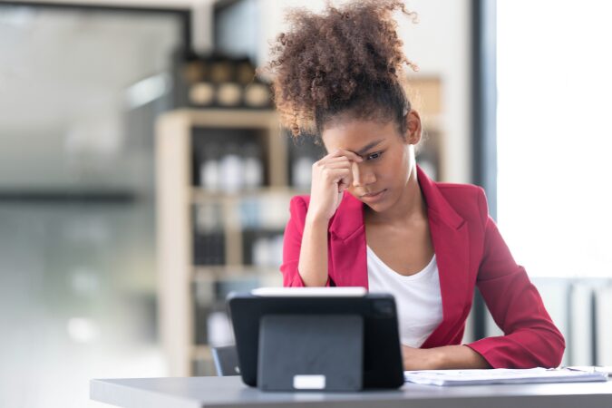 Mulher preocupada analisando relatórios e dados em planilhas no tablet.