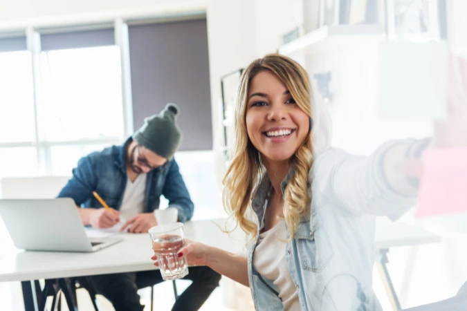 Profissional sorridente organizando post-its coloridos enquanto trabalha com a equipe, representando uma rotina de trabalho leve e produtiva.