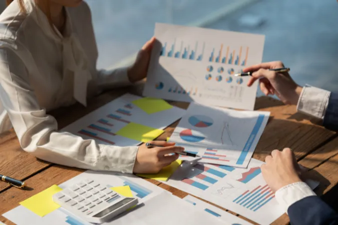 Duas pessoas revisando gráficos e planilhas com calculadora para medir a margem líquida da empresa
