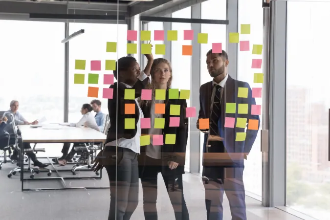 Equipe reunida em frente a um quadro de vidro com post-its coloridos, planejando tarefas com metodologia Kanban