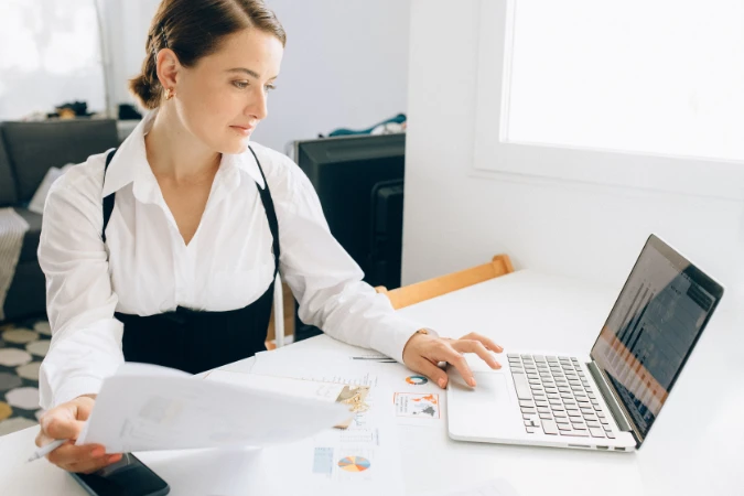 Mulher analisando relatórios financeiros e gráficos em notebook durante processo de gestão financeira estratégica.