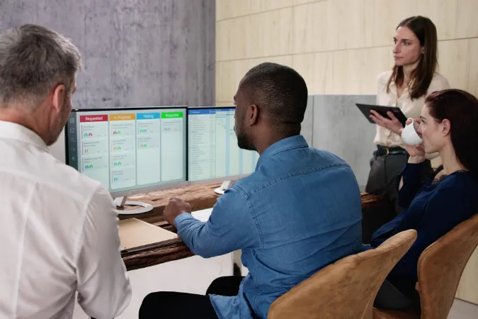 Equipe de projetos utilizando software de gestão em tela dupla para acompanhar backlog e Sprints no Scrum