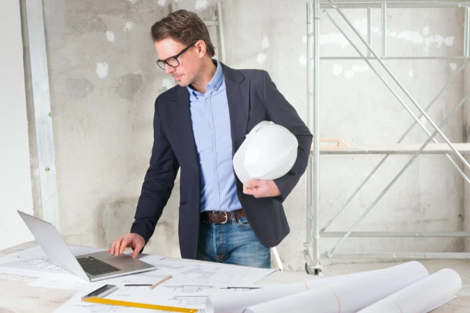 Engenheiro analisando planta e cronograma em notebook em ambiente de obra