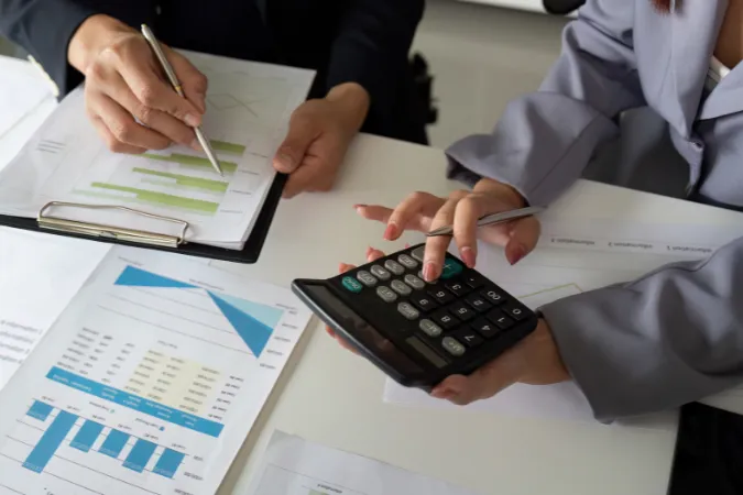 Gestores utilizando relatórios e calculadora para avaliar indicadores de desempenho financeiro.