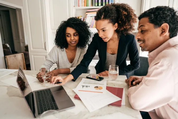 Equipe reunida em frente ao laptop analisando relatórios financeiros e discutindo estratégias de negócios.