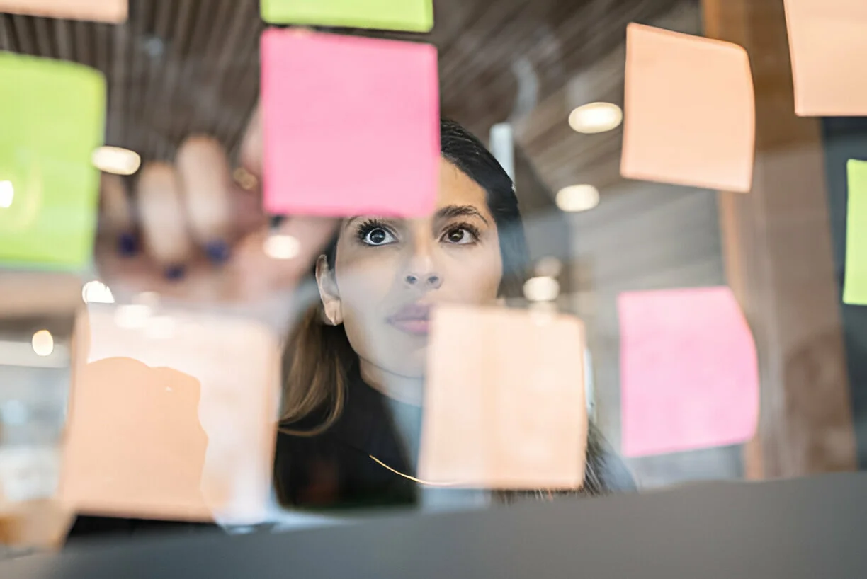 Mulher gerente de projetos analisando post-its coloridos em um quadro de planejamento