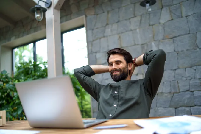 Empresário satisfeito relaxando em frente ao laptop após organizar as finanças com software de gestão.