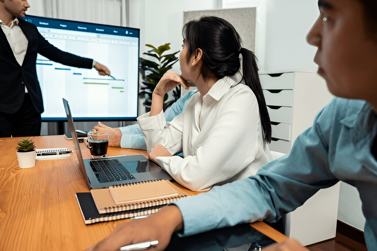 Reunião de trabalho com apresentação de gráfico de Gantt projetado na tela para acompanhamento de cronograma.