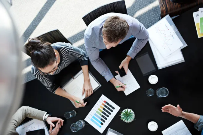 Vista aérea de equipe analisando gráficos e documentos em uma reunião de planejamento