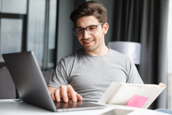 Homem sorridente usando notebook e caderno para planejar finanças com apoio de software de gestão.
