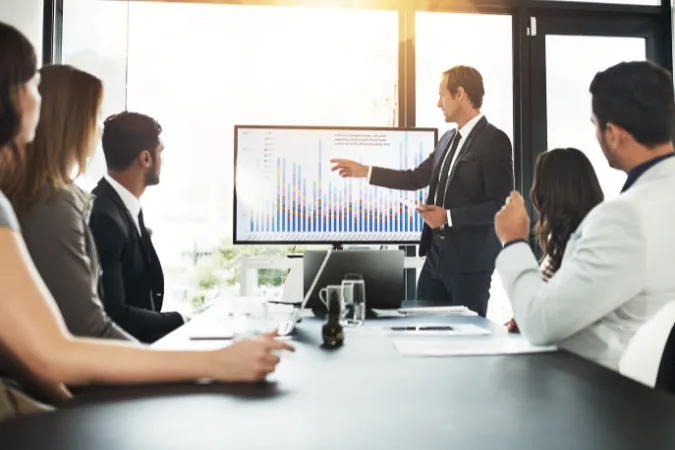 Executivos analisando gráficos em relatórios impressos e digitais durante reunião de negócios.