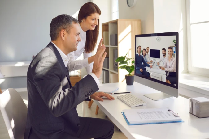 Colaboradores remotos interagindo por videoconferência com colegas no escritório em modelo de time híbrido.