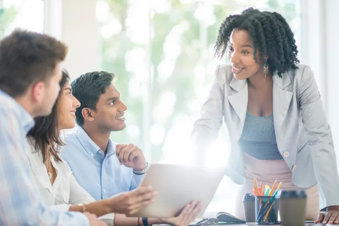 Líder sorridente interagindo com equipe durante reunião de planejamento com laptops.