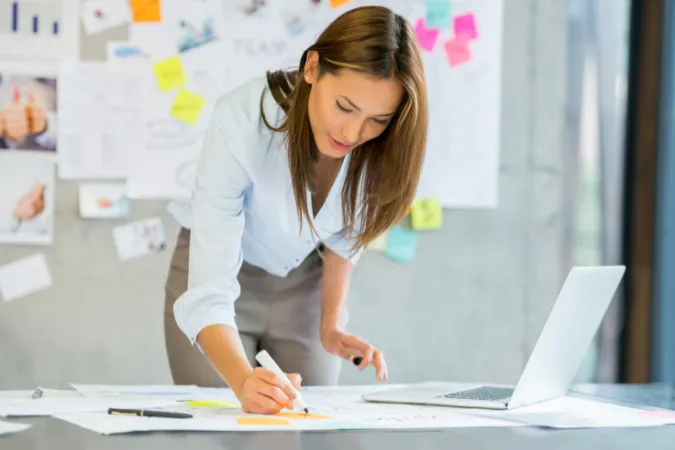 Mulher organizando anotações em mesa de trabalho com laptop aberto, representando o uso de ferramentas como o FlowUp para gestão de prioridades