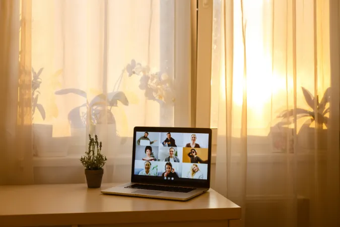 Notebook com videochamada em grupo sobre uma mesa iluminada pelo sol