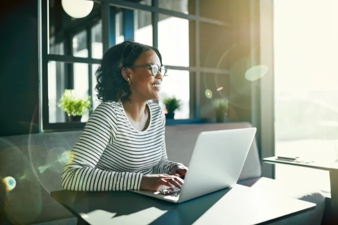 Mulher sorridente utilizando notebook em ambiente iluminado para gerenciar as finanças da empresa