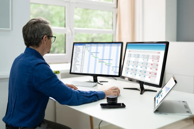 Profissional gerenciando cronograma de obra em softwares com gráficos de Gantt e calendário.
