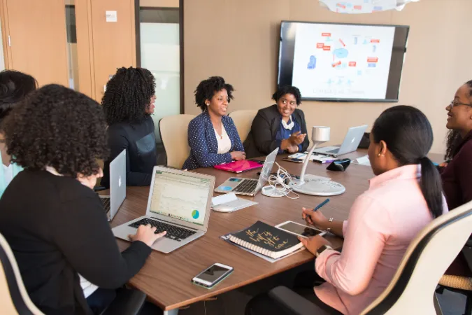 Grupo de profissionais reunidos em sala de reunião com laptops e apresentações na tela.