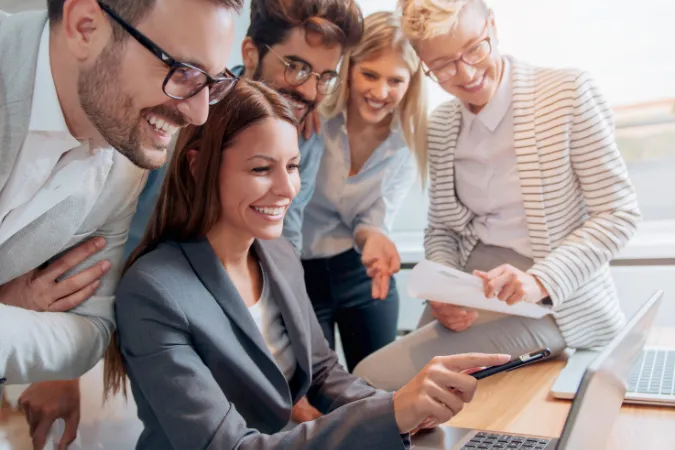 Grupo de profissionais sorrindo e analisando juntos informações em um laptop