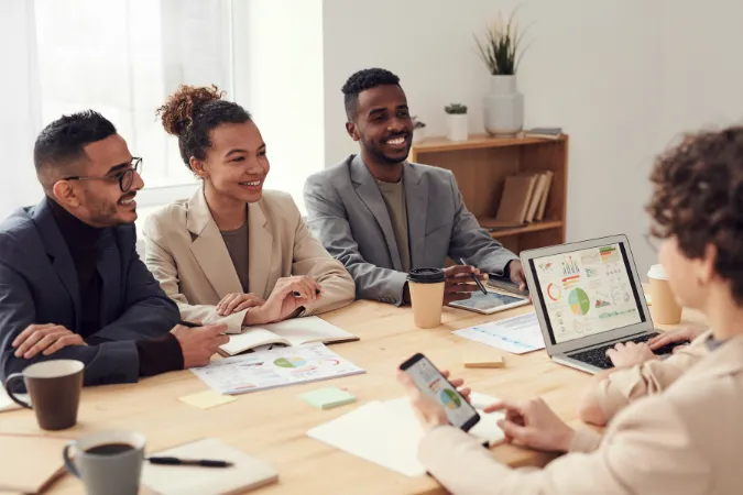 Equipe de profissionais em reunião analisando gráficos em laptop e relatórios impressos.