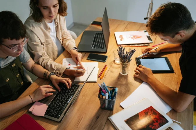 Equipe trabalhando em conjunto com laptops e tablet para organizar tarefas, documentos e atividades de projetos.
