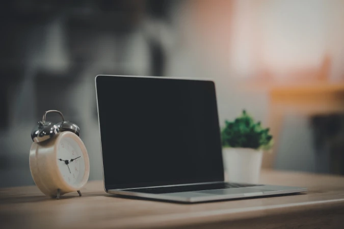 Notebook sobre mesa ao lado de relógio analógico representando controle de tempo e gestão de projetos
