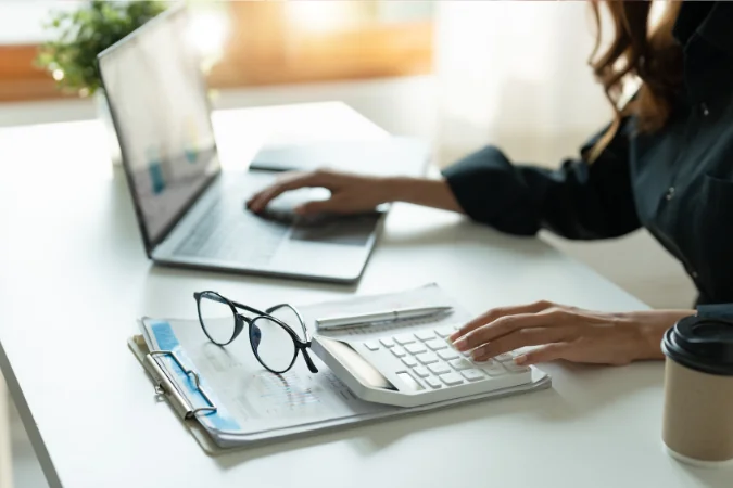 Mãos usam calculadora ao lado de notebook e relatórios, registrando horas e resultados para Autogestão.