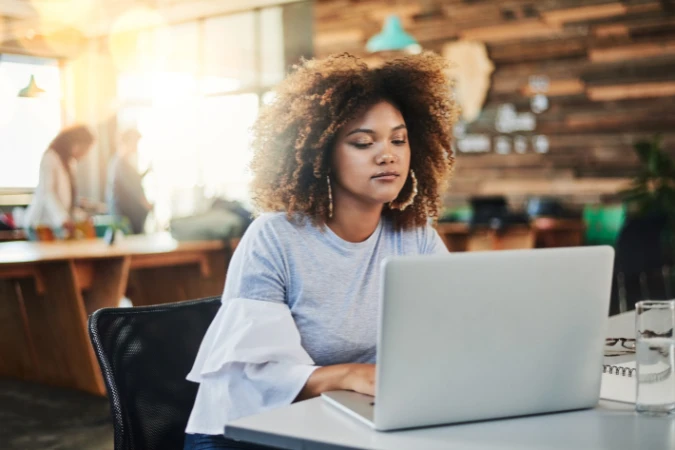 Mulher jovem trabalhando concentrada em um café moderno, representando o deep work mesmo em ambientes colaborativos.