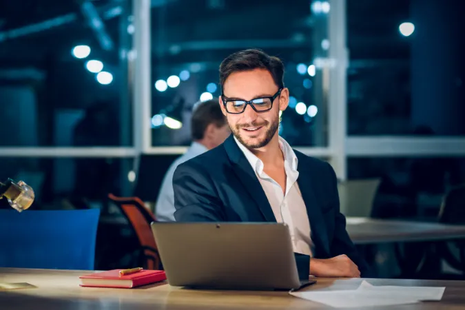 Profissional sorridente analisando um projeto no notebook, utilizando software de gestão com cronogramas e relatórios.