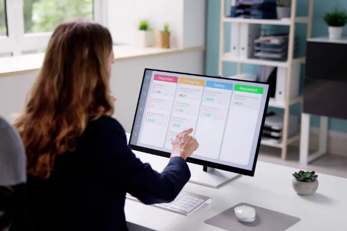Profissional usando um sistema digital com colunas de Kanban visíveis na tela do computador