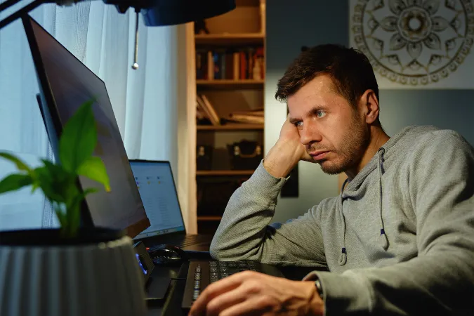 Homem em home office com expressão de desânimo olhando para o computador