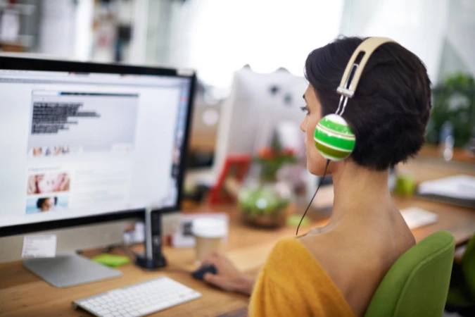 Profissional usando fones de ouvido e computador em ambiente de trabalho criativo, mantendo concentração para entrar no estado de flow.