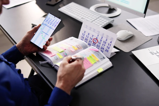 Profissional ajustando tarefas no planner e no celular ao mesmo tempo, mostrando o planejamento diário com o método Timeboxing.