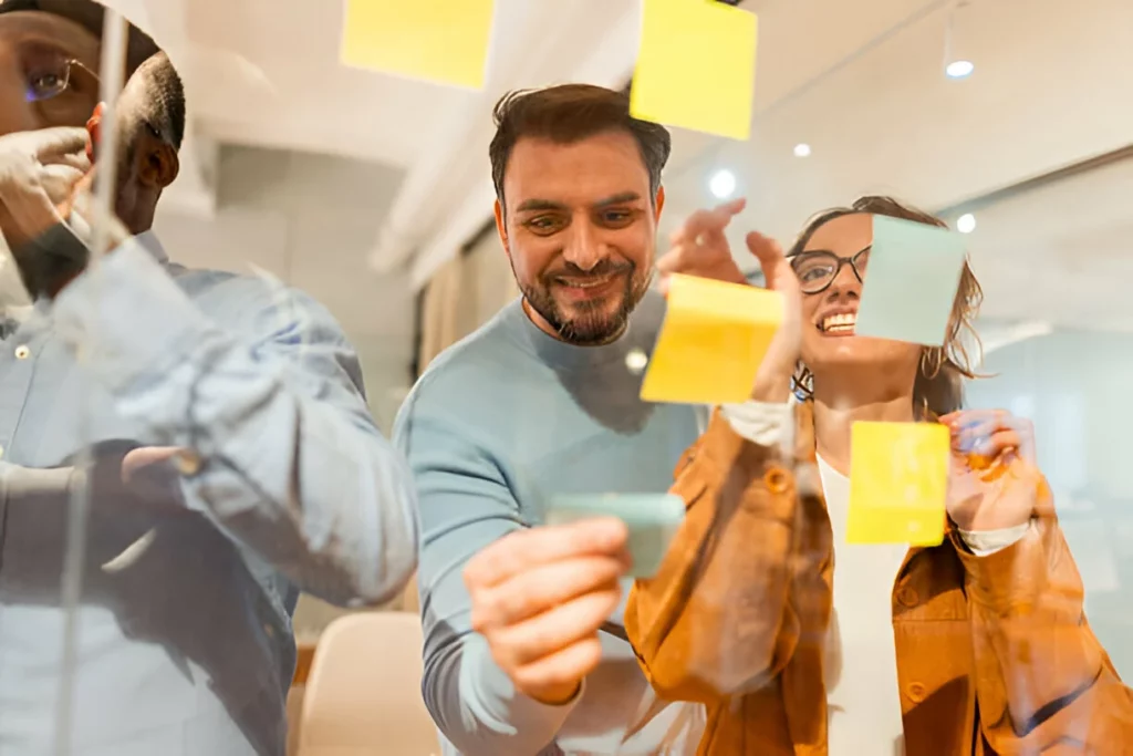 Grupo de web designers usando notas pegajosas em uma parede de vidro durante uma reunião