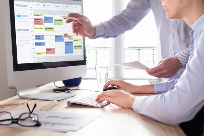 Duas pessoas analisando calendário digital colorido para planejar tarefas e compromissos