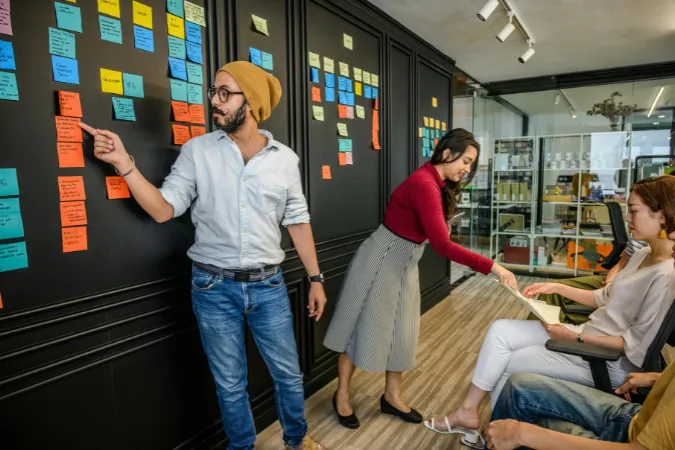 Profissionais organizando tarefas em um quadro cheio de post-its coloridos, simulando a integração entre Waterfall e Scrum.