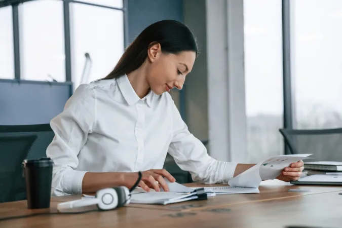 Mulher concentrada revisando documentos e planejando atividades diárias no ambiente de trabalho.