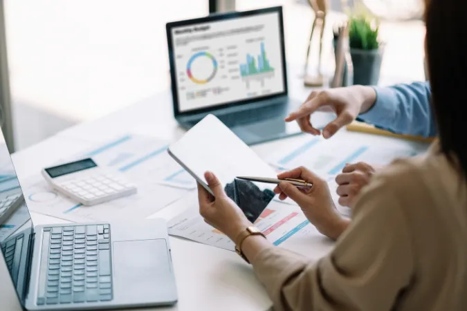 Profissionais analisando relatórios financeiros e gráficos em laptop para identificar inadimplências.
