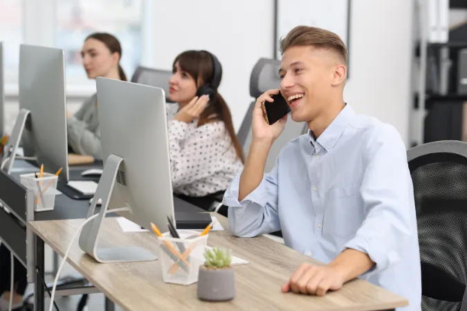 Jovem atendente falando ao telefone em escritório, representando a importância da comunicação para prevenir inadimplências.