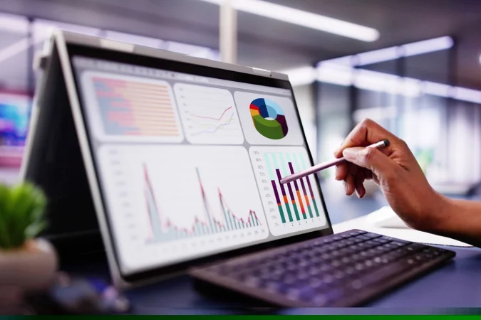 Tela com dashboard de gráficos e indicadores sendo analisada por profissional com caneta apontando dados