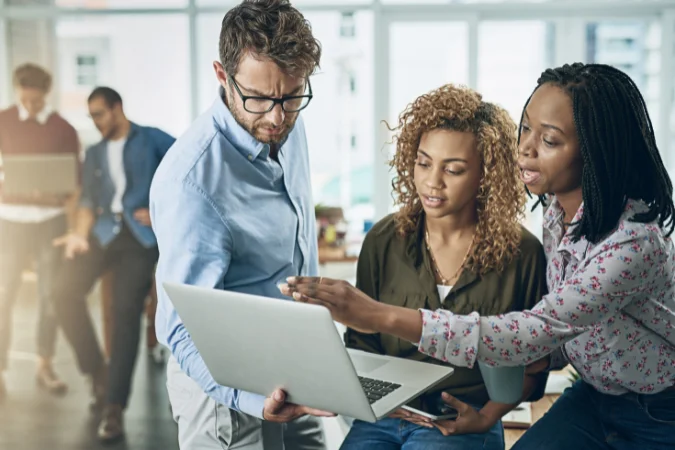 Profissionais reunidos em uma mesa usando computadores para planejar e revisar processos automatizados.
