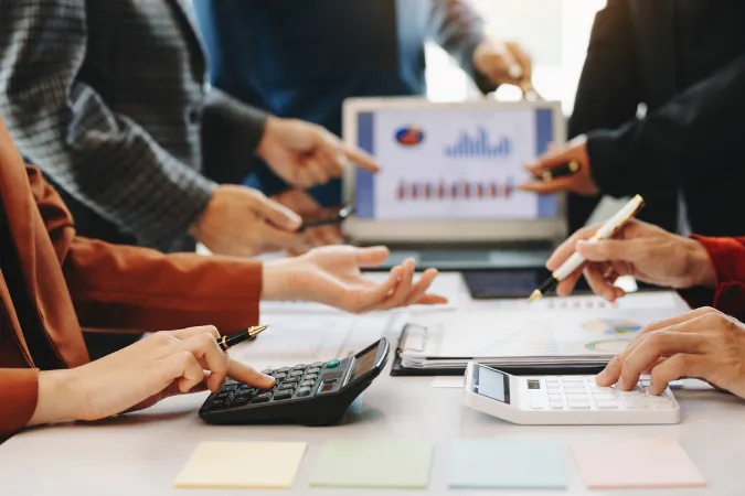 Grupo de profissionais analisando gráficos e calculadoras em mesa de reunião, simbolizando os desafios financeiros causados pela falta de software de gestão.