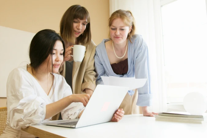 Grupo de profissionais colaborando em torno de um notebook e discutindo planos de projeto.
