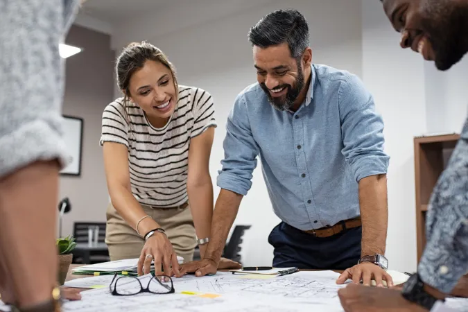 Arquitetos sorrindo e discutindo projetos sobre a mesa, simbolizando como metas claras e bem definidas aumentam produtividade sem comprometer o bem-estar.