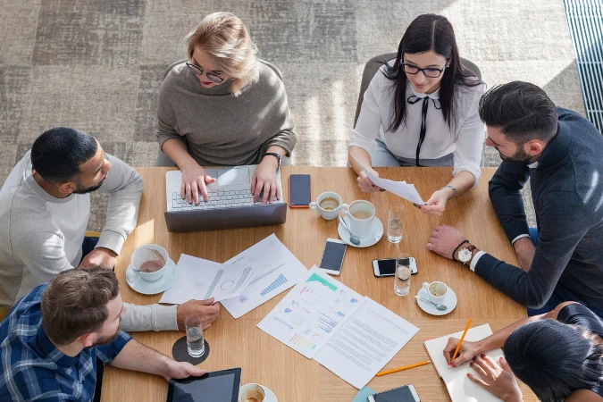 Equipe reunida em mesa de trabalho avaliando gráficos e relatórios de projeto com abordagem ágil.