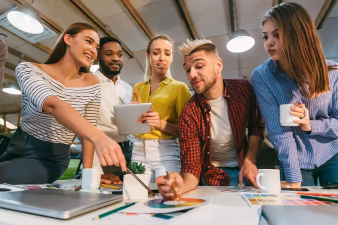Grupo de designers discutindo paleta de cores e protótipos em uma mesa de trabalho colaborativo.
