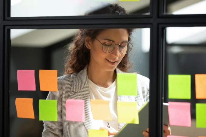 Profissional analisando tarefas e notas adesivas coloridas em um quadro de planejamento ágil.