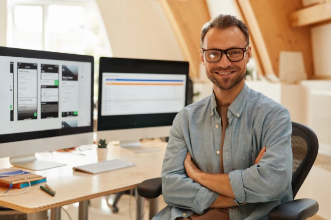 Profissional satisfeito em frente ao computador com dashboards de software de gestão na tela.