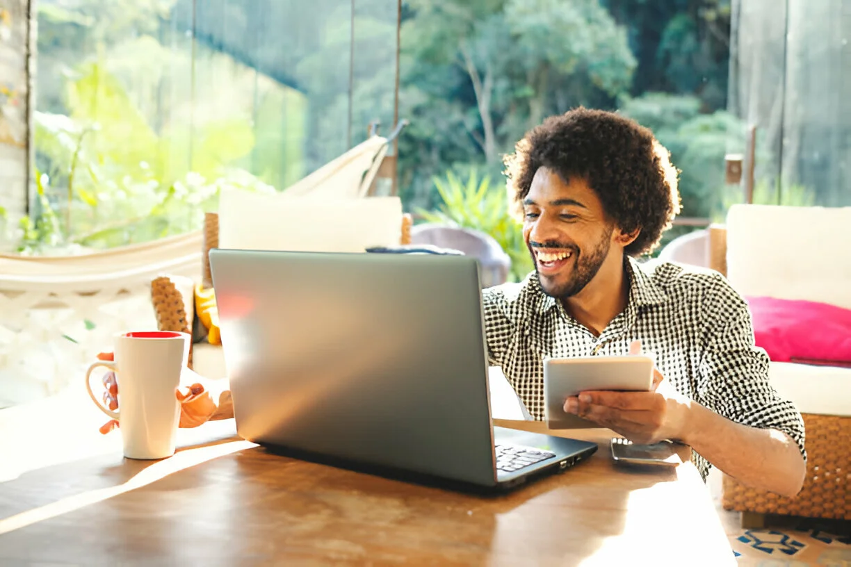 Profissional utilizando laptop e tablet em home office com ferramentas para trabalho remoto.