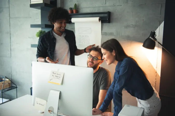Equipe de três pessoas discutindo protótipos de projeto em frente a um monitor com layout de software